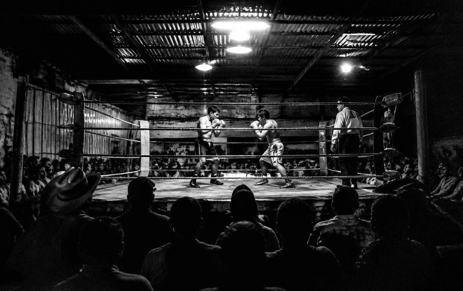 Ring de boxeo amateur rodeado de público durante una función nocturna